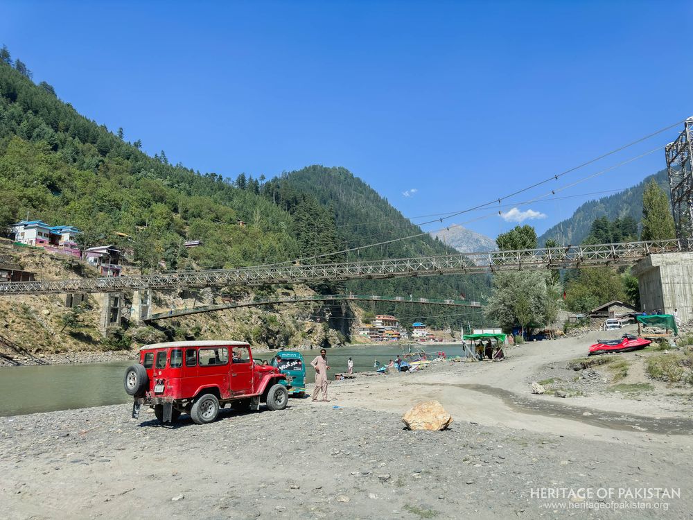 A bright red truck rests near the riverbank beneath Sharda's striking suspension